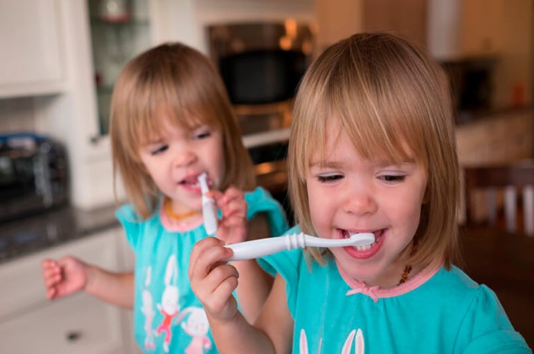 Twin girls brushing teeth together